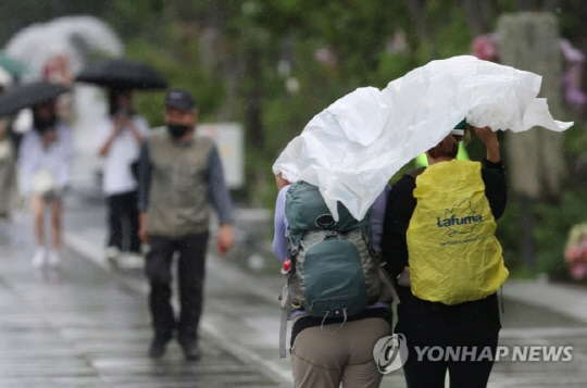 서울 광화문광장을 지나는 시민들이 갑자기 쏟아지는 비에 비닐을 쓴 채 걸어가고 있다. 사진 연합뉴스