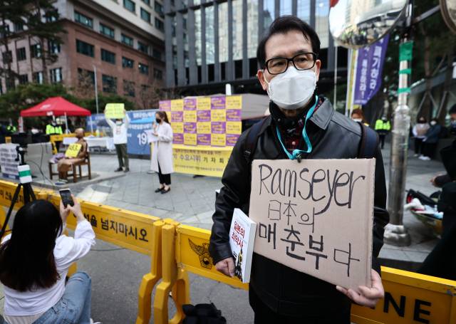 ▲ 2021년 3월 17일서울 종로구 옛 일본대사관 앞에서 열린 제1483차 일본군성노예제 문제해결을 위한 정기 수요시위 기자회견에서 한 시민이 마크 램지어 하버드 로스쿨 교수를 비난하는 내용의 손 피켓을 들어 보이고 있다. ⓒ연합뉴스