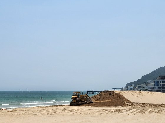 지난 19일 부산 송정해수욕장에서 중장비가 모래 평탄화 작업을 하고 있다. 당초 해운대구는 강서구에서 낙동강 어선 통학로 준설 사업 때 나온 모래로 유실된 백사장을 채울 예정이었으나 주민 반발로 무산되자 이날 파낸 백사장 구덩이 위쪽으로 모래를 덮고 있다. 위성욱 기자