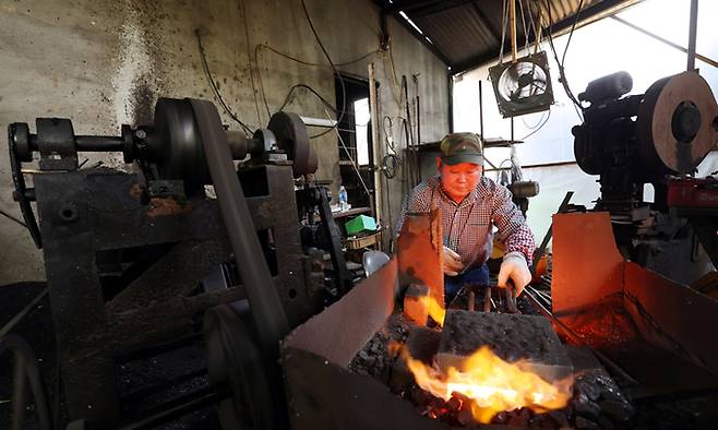 1000도가 넘는 고열의 가마 앞에서 전통 끌 김원태 장인이 50년 세월을 함께한 구식 단조기 앞에서 철근을 불에 달구어 끌의 모양을 만드는 첫 작업인 단조작업을 하고 있다. 장시간 작업으로 장인의 얼굴이 벌겋다.