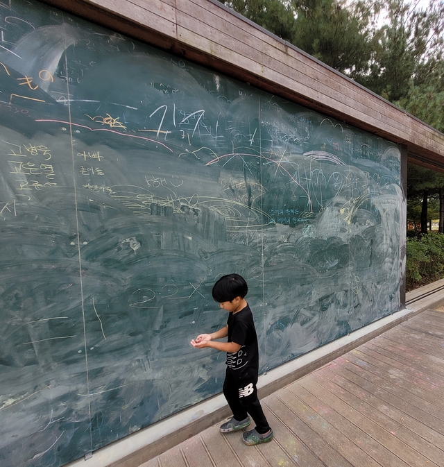 한 아이가 슬라이딩 가벽 형태로 조성된 맘껏숲놀이터 내 대형 칠판에 분필로 그림을 그리고 있다. 문정임 기자