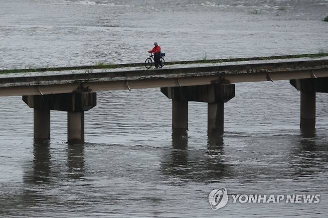 수위 높아지는 중랑천 (서울=연합뉴스) 김주성 기자 = 서울 동북·서북권에 호우주의보가 발효된 11일 수위가 급격히 높아지고 있는 중랑천의 살곶이 다리를 한 시민이 자전거를 끌고 건너고 있다. 2023.7.11 utzza@yna.co.kr