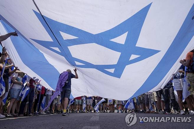 이스라엘 국기를 떠받친 채 사법정비 입법에 저항하는 시위대. [AP 연합뉴스 자료사진. 재판매 및 DB 금지]