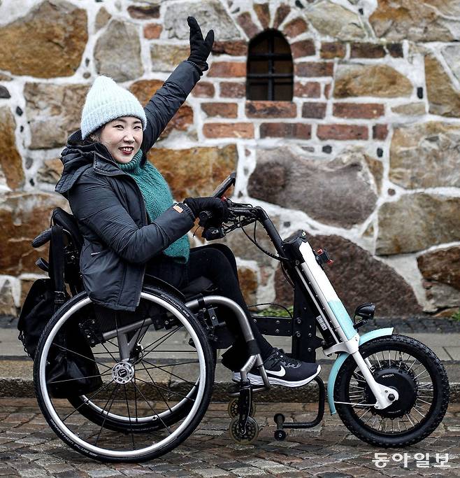 가구 디자이너 김예솔 씨가 3월 22일 스웨덴 남부 도시 룬드 거리에서 손을 활짝 들어 보였다. 김 씨는 휠체어 앞에 특수 제작된 동력장치를 결합해 오토바이를 타듯 자유롭게 시내를 누볐다.