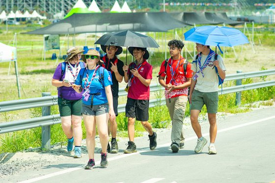 지난 1일 전북 부안군 새만금 부지 내 세계잼버리에서 스카우트 대원들이 양산으로 더위를 피하며 걸어가고 있다. 사진 세계스카우트연맹