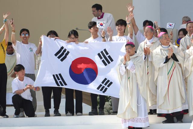 포르투갈 리스본의 테주 공원에서 열린 올해 가톨릭 세계청년대회 폐막 미사에서 2027년 차기 대회 개최지가 서울로 발표되자 한국의 순례자들과 주교들이 무대 위에서 태극기를 펼쳐 들며 환호하고 있다. 리스본= AFP 연합뉴스