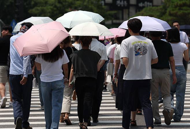 지난달 21일 전국적으로 무더운 날씨가 이어진 가운데 시민들이 서울 광화문사거리에서 우산과 양산을 쓴 채 횡단보도를 건너고 있다./연합뉴스