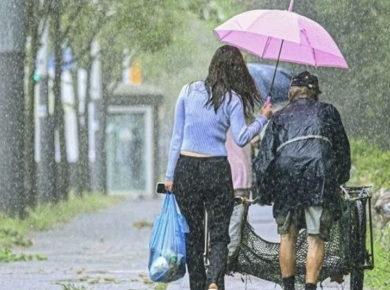 지난 달 29일 한 여성이 비를 맞으며 빈 수레를 끌고 가는 노인에게 우산을 씌어주고 함께 걷고 있다. / 사진=경기일보