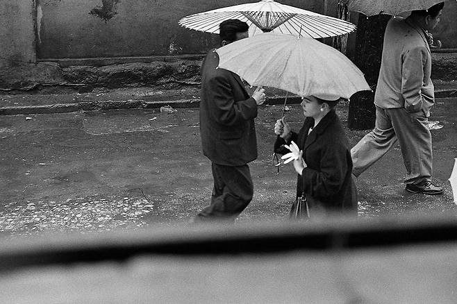 C컷/ 서울 명동, 1956-1963. 비 오는 서울 명동 거리, 우산을 쓴 여성 옆을 양복입은 남자가 지나가며 보고 있다./ 사진가 한영수