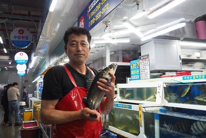 수암회수산시장에서 친절하기로 소문난 해강수산 사장님이 싱싱한 농어를 붙잡아 기자에게 보여주고 있다. 사진=최수상 기자