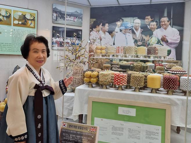 민속주 안동소주 제조부문 배경화 무형문화재가 안동소주전통음식박물관에 진열된 고 엘리자베스 영국여왕 생일상차림을 설명하고 있다. 배 여사는 1999년 영국여왕의 안동 방문 때 시어머니인 고 조옥화 여사와 함께 이 생일상을 직접 차렸다. /박순욱 기자