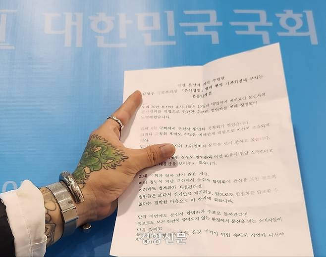 한 타투노동자가 지난달 18일 ‘문신업법’ 발의를 환영하는 기자회견을 하기 위해 국회 소통관을 찾아 기자회견문을 들어 보이고 있다. 이두리 기자