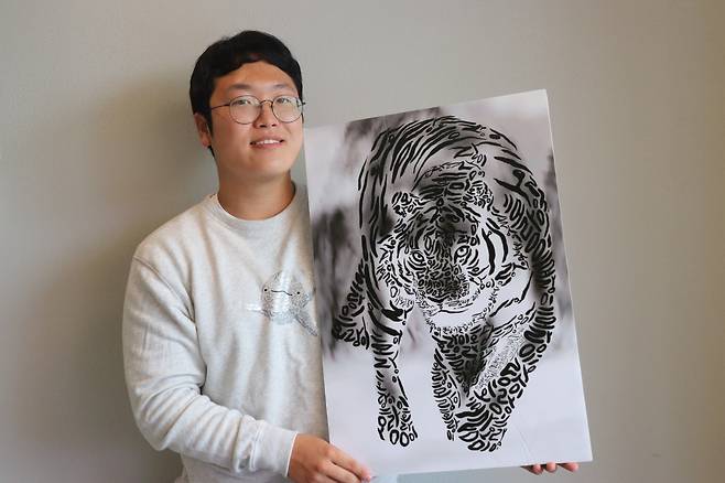 9일 '한글화가' 진관우 작가가 서울 용산구의 한 카페에서 진행된 본지 인터뷰에서 자신이 그린 호랑이 그림을 들어 보이고 있다. 이 그림에서 호랑이의 몸통은 '호랑이'라는 세 글자만으로 채워져 있다. /조재현 기자