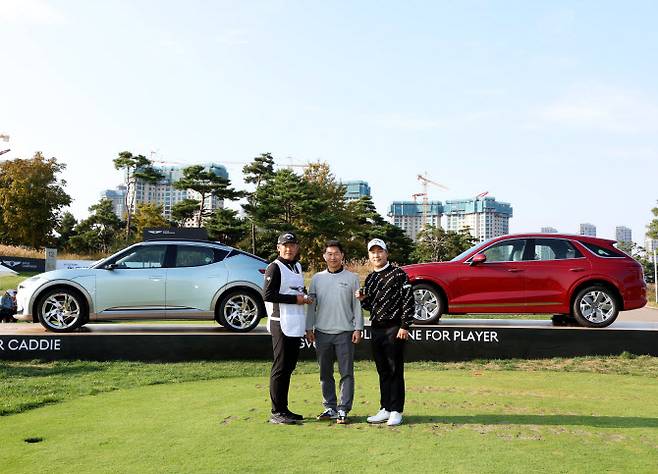 왼쪽부터 정준호 캐디, 송민규 제네시스사업본부장 부사장, 전가람이 홀인원 부상인 GV70 전동화 모델과 GV60 앞에서 기념촬영을 하는 모습(사진=제네시스 챔피언십 조직위 제공)