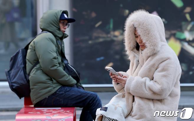 영하권 추위가 이어진 12일 오전 서울 중구 명동거리를 찾은 관광객들이 두꺼운 외투를 입은 채 자리에 앉아 있다. 2023.11.12/뉴스1 ⓒ News1 장수영 기자