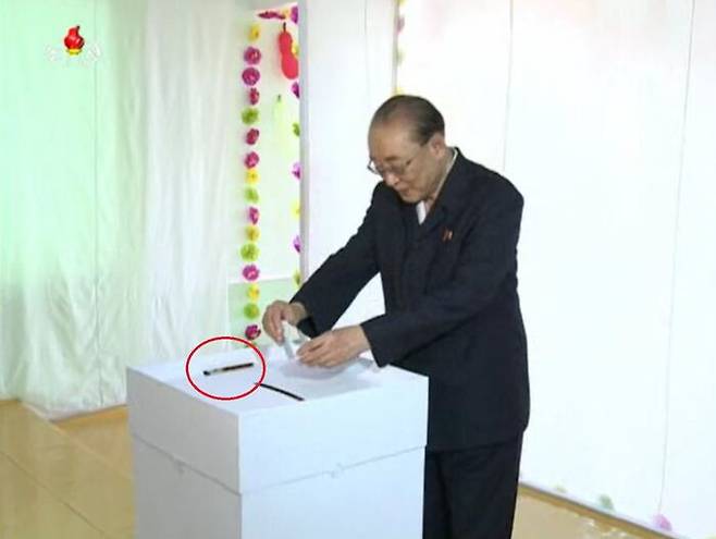 투표실에서 투표하는 투표자, 투표함 위에 볼펜(빨간 원)이 놓여져 있다. (조선중앙TV, 2015년 7월)