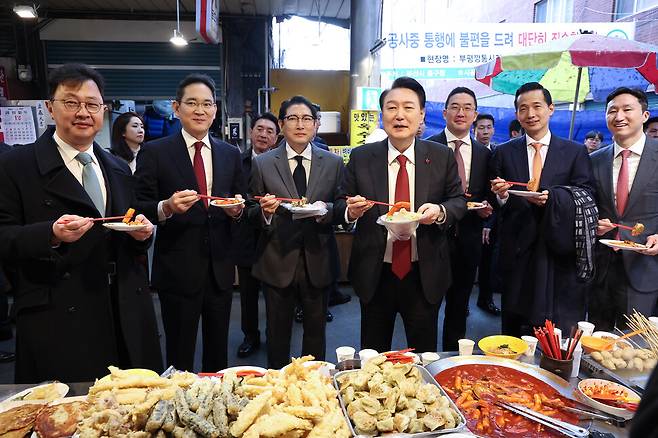 윤석열 대통령이 6일 부산 중구 깡통시장에서 기업 총수들과 함께 떡볶이 튀김 빈대떡을 시식하고 있다. 오른쪽 부터 정기선 HD현대 부회장, 김동관 한화그룹 부회장, 구광모 LG그룹 회장, 윤 대통령, 조현준 효성그룹 회장, 이재용 삼성전자 회장, 최재원 SK수석부회장. 부산/연합뉴스