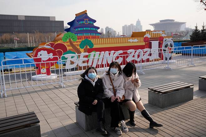 지난 18일 중국 베이징에서 마스크를 쓴 여성들이 2022 베이징 동계 올림픽 개최를 알리는 조형물 앞 벤치에 앉아 있다. 코로나 팬데믹 여파로 일대가 이전보다 한산하다. /AP 연합뉴스
