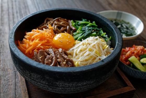 Traditional bibimbap topped with a variety of sauteed and seasoned vegetables and a egg yolk, served in a hot stone pot. [SHUTTERSTOCK]