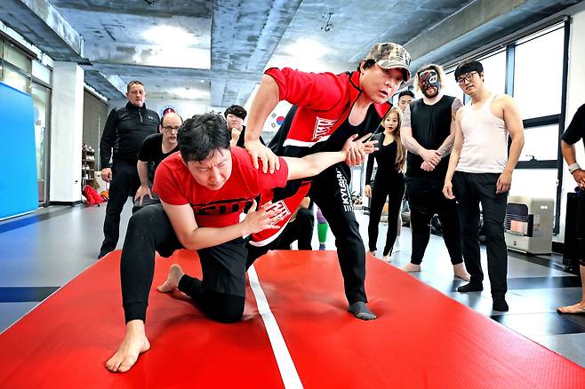 지난 16일 오전 평택의 한 도장에서 일본의 다지리 선수가 한국 PWS 소속 프로레슬러 시호의 어깨를 누르며 공격 기술에 대해 설명하고 있다. 뒤쪽에는 진지하게 경청하는 현역 선수 및 일반 연습생들이 보인다. /주민욱 영상미디어 기자