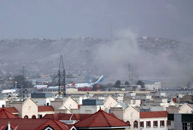 비행기 뒤로 자욱한 연기 - 26일(현지 시각) 아프가니스탄 카불의 하미드 카르자이 국제공항 근처에서 폭발로 인한 연기가 피어오르고 있다. 미 국방부는 이날 카불 공항 밖에서 폭발이 있었다고 밝혔다. 외신들은 이번 폭발이 자살 폭탄 테러로 추정된다며 최소 13명이 사망했다고 전했다. /AP 연합뉴스