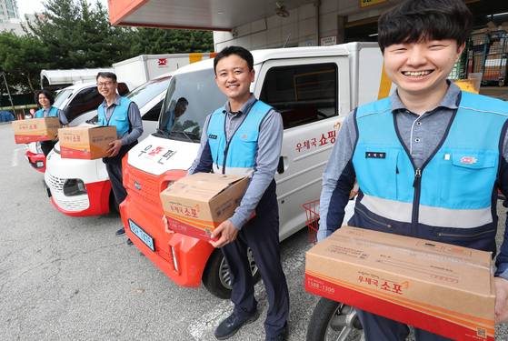 Korea Post employees smile in front of their delivery vehicles. [KOREA POST]