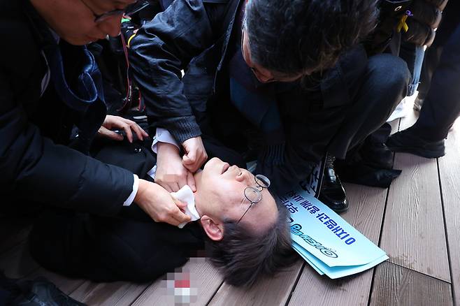 더불어민주당 이재명 대표가 2일 부산 가덕도 신공항 부지를 둘러본 후 기자들과 문답을 진행하던 중 왼쪽 목 부위에 습격을 당해 피를 흘린 채 쓰러져 있다. 연합뉴스