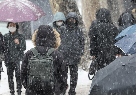 Commuters walk near Hyehwa Station in central Seoul as heavy snow falls in the area on Tuesday morning. [YONHAP]