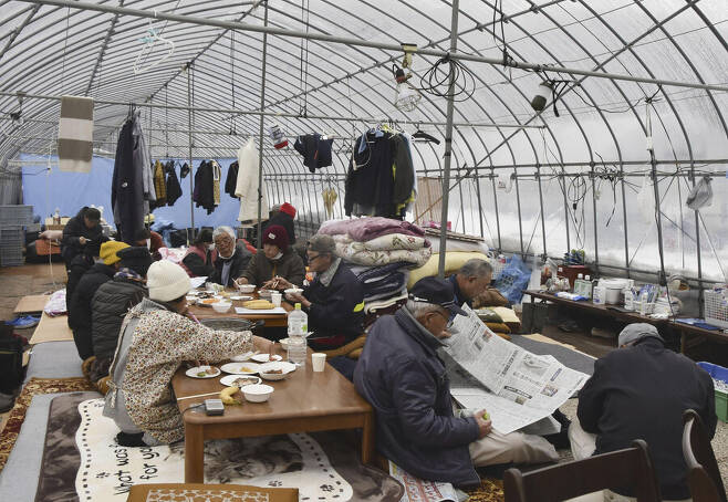 새해 첫날 일본 혼슈 중부 이시카와현 노토반도에서 발생한 규모 7.6의 강진으로 집이 무너진 일부 주민들이 공식 대피소가 부족해 인근 농업용 비닐하우스에서 생활하고 있다. 지난 11일 같이 밥을 먹고 있는 모습. AP 연합뉴스