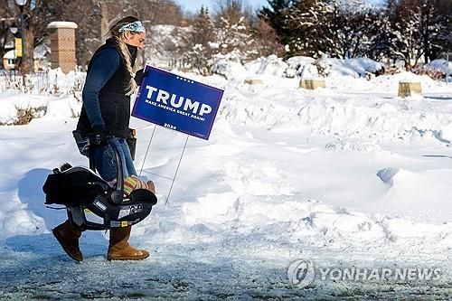 아이오와 코커스를 하루 앞둔 14일(현지시간) 도널드 트럼프 전 대통령의 지지자 한명이 트럼프의 이름이 쓰인 피켓을 들고 유세장으로 향하고 있다. [사진출처=AFP 연합뉴스]
