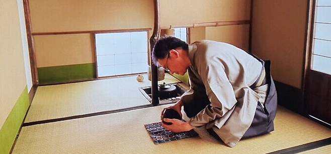 기모노 차림으로 무릎을 꿇고 앉아 다완을 감상하는 다인의 모습. &nbsp;