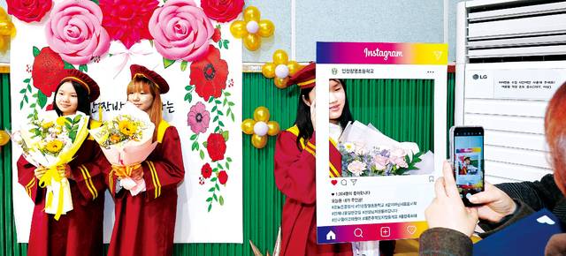 과거 졸업식 사진은 학교가 배경이었지만 요즘은 화려한 포토월이 필수다. 4일 인천 동구 창영초등학교 졸업생들이 꽃으로 꾸민 포토월(왼쪽)과 사회관계망서비스(SNS)인 인스타그램 판지를 배경으로 기념사진을 찍고 있다. 연합뉴스
