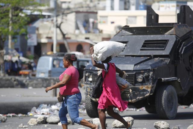 아이티 여성들이 지난 7일 수도 포르토프랭스의 한 거리에서 무장한 경찰차 앞을 빠르게 지나가고 있다. 포르토프랭스=AP 연합뉴스
