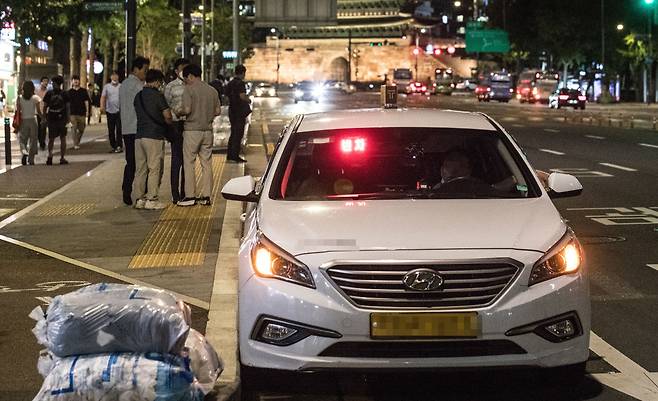 11일 오후, 서울 중구 시청역 인근에서 퇴근한 직장인들이 ‘빈차’ 표시등이 뜬 택시 뒤로 택시를 기다리고 있다. 코로나 사태를 거치며 법인 택시 회사의 구인난, 개인택시 기사의 고령화 등 택시 업계 내 구조적 문제가 심화되고, 배달과 택배업으로 인력이 몰리면서 전국 주요 대도시에서는 최근 ‘야간 택시 대란’으로 시민 불편이 커지고 있다. 2022.7.11 / 고운호 기자