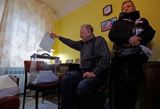 11일(현지시간) 러시아가 장악한 우크라이나 도네츠크에서 러시아 대선 선거관리위원회 위원들이 지역 주민들을 방문한 가운데 한 남성이 자신의 집에서 이동식 투표함에 접지 않은 투표용지를 넣고 있다. 로이터=연합뉴스