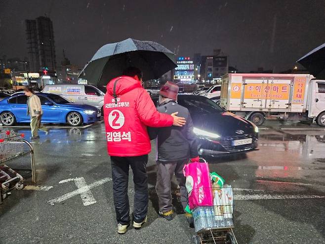 김영석 국민의힘 아산갑 후보가 장을 보고 이동하는 지역 주민이 비를 맞지 않도록 우산을 씌워주고 있다. ⓒ김영석 캠프