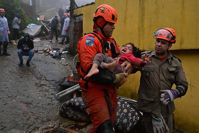 23일(현지시간) 브라질 리우데자네이루주 페트로폴리스에서 폭우로 무너진 집에서 구조된 4세 여아를 구급대원들이 옮기고 있다. AFP=연합뉴스