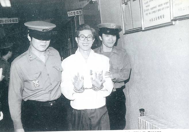 1986년 12월 보도지침 사건으로 구속 기소된 신홍범 기자가 재판을 받기 위해 법정으로 들어서며 방청나온 동료들에게 묶인 손을 들어 인사하고 있다. /조선투위 제공