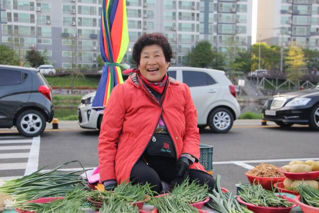 ▲ 원주 새벽시장에서 20년간 농산물을 판매해 온 진수정(70)씨가 직접 재배한 농산물을 앞에 두고 환한 웃음을 짓고 있다.