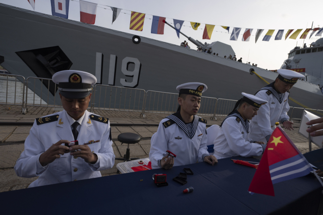 지난 20일 중국 산둥성 칭다오에서 해군 창설 75주년을 맞아 중국 유도탄 구축함 구이양 앞에서 선원들이 방문객들을 위한 기념품을 준비하고 있다. AP연합뉴스