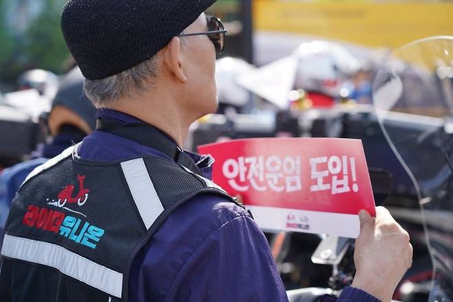 공공운수노조 라이더유니온지부 주최로 지난 25일 서울 송파구 우아한형제들 빌딩 앞에서 열린 7회 라이더 대행진에 참가한 한 조합원이 안전운임 도입을 요구하는 손팻말을 들고 있다. 라이더유니온지부 제공