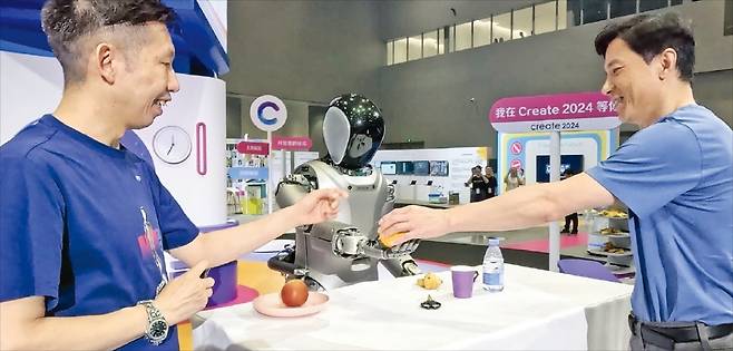 < 오렌지 건네는 로봇 > 유비테크의 휴머노이드 ‘워커S’가 지난달 16일 중국 선전에서 열린 바이두 인공지능(AI) 개발자 대회에서 리옌훙 바이두 최고경영자(CEO·오른쪽)에게 오렌지를 건네고 있다. 리 CEO가 “오렌지를 달라”고 하자 워커S는 오렌지를 정확히 식별한 후 손으로 집어 건넸다.  /유비테크 제공