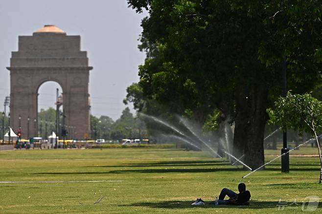 25일(현지시간) 인도 뉴델리의 인디아게이트 앞 잔디밭에서 한 남성이 나무 밑 그늘에 누워 휴식을 취하고 있다. 2024.04.25 ⓒ AFP=뉴스1 ⓒ News1 정지윤 기자