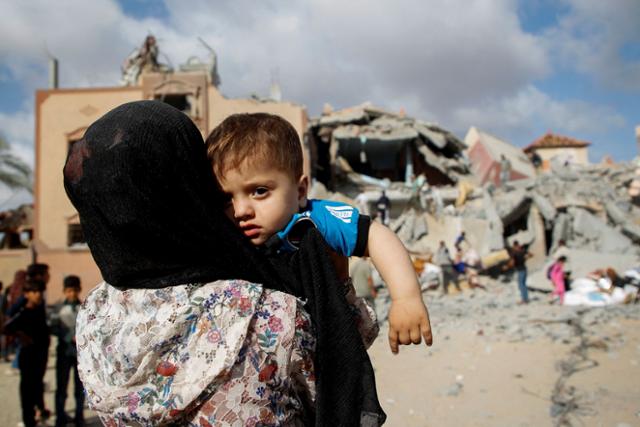5일 가자지구 최남단 라파에서 이스라엘의 공격으로 파괴된 건물을 배경으로 한 팔레스타인 주민이 어린이를 안고 있다. 라파=로이터 연합뉴스