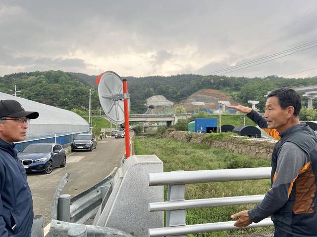 이강락 양산마을 이장(오른쪽)이 멀리 뒤편으로 보이는 고속국도 공사현장을 배경으로 이번 침수 피해의 원인에 대해 설명하고 있다.