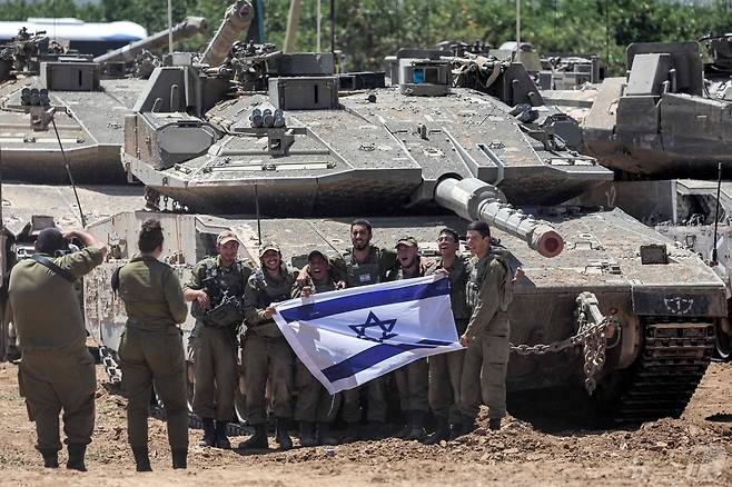 이스라엘군인들이 9일(현지시간) 이스라엘 국기를 펼쳐들고 남부 가자 접경지에 집결된 메르카바 전차앞에서 사진을 찍고 있다. 남다른 덩치의 메르카바 전차는 세계에서 방호력이 가장 우수한 탱크로 평가된다. 2024.05.09 ⓒ AFP=뉴스1 ⓒ News1 권진영기자