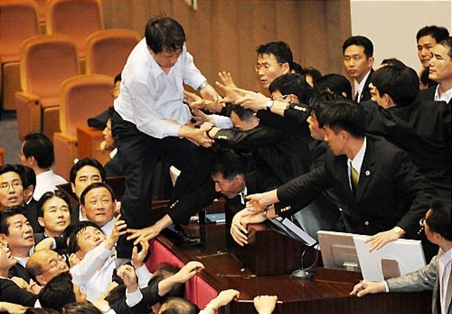 2009년 7월 22일 여야의 난투극 속에 열린 국회 본회의에서 이윤성 국회 부의장이 김형오 국회의장 대신 미디어법을 통과시키자 민주당 조정식 의원이 이에 항의하며 셔츠 차림으로 본회의장 단상에 올라가고 있다. /뉴시스