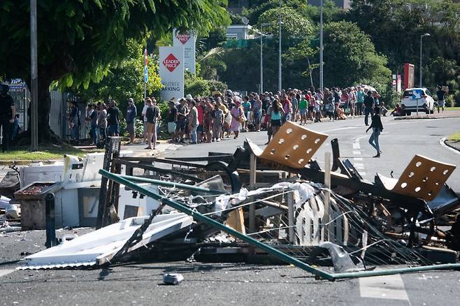 13일(현지시간)부터 시작된 프랑스령 뉴칼레도니아의 폭력 소요 사태로 불에 탄 물건들이 도로를 점령한 가운데 현지 주민과 관광객들이 식량을 구입하기 위해 길게 줄을 서고 있다. /AFPBBNews=뉴스1