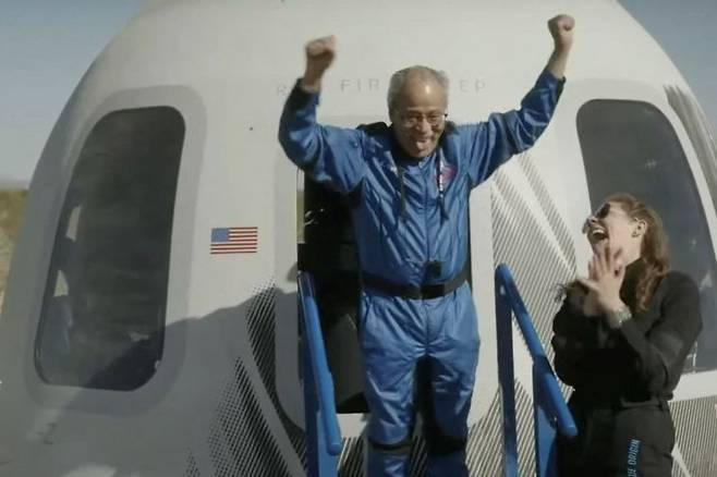미국 전직 파일럿이자 1960년대 최초의 흑인 우주비행사 후보였던 에드 드와이트씨가 19일(현지시간) 미 텍사스주 밴 혼 발사장 인근에 착륙한 우주선 캡슐에서 걸어 나오며 두 팔을 번쩍 들고 있다. [이미지출처=AFP 연합뉴스]