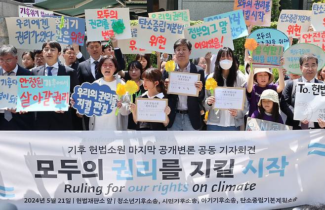 한국 정부의 기후변화 대응이 헌법에 합치하는지를 묻는 기후소송 두번째 공개 변론이 열린 21일 오후 서울 종로구 헌법재판소 앞에서 기후소송 원고 단체와 공동 대리인단이 기자회견을 열어 구호를 외치고 있다. 참가자들은 ‘반드시 행복은 오고야 만다’는 꽃말의 마리골드를 직접 접어 들었다. 백소아 기자 thanks@hani.co.kr